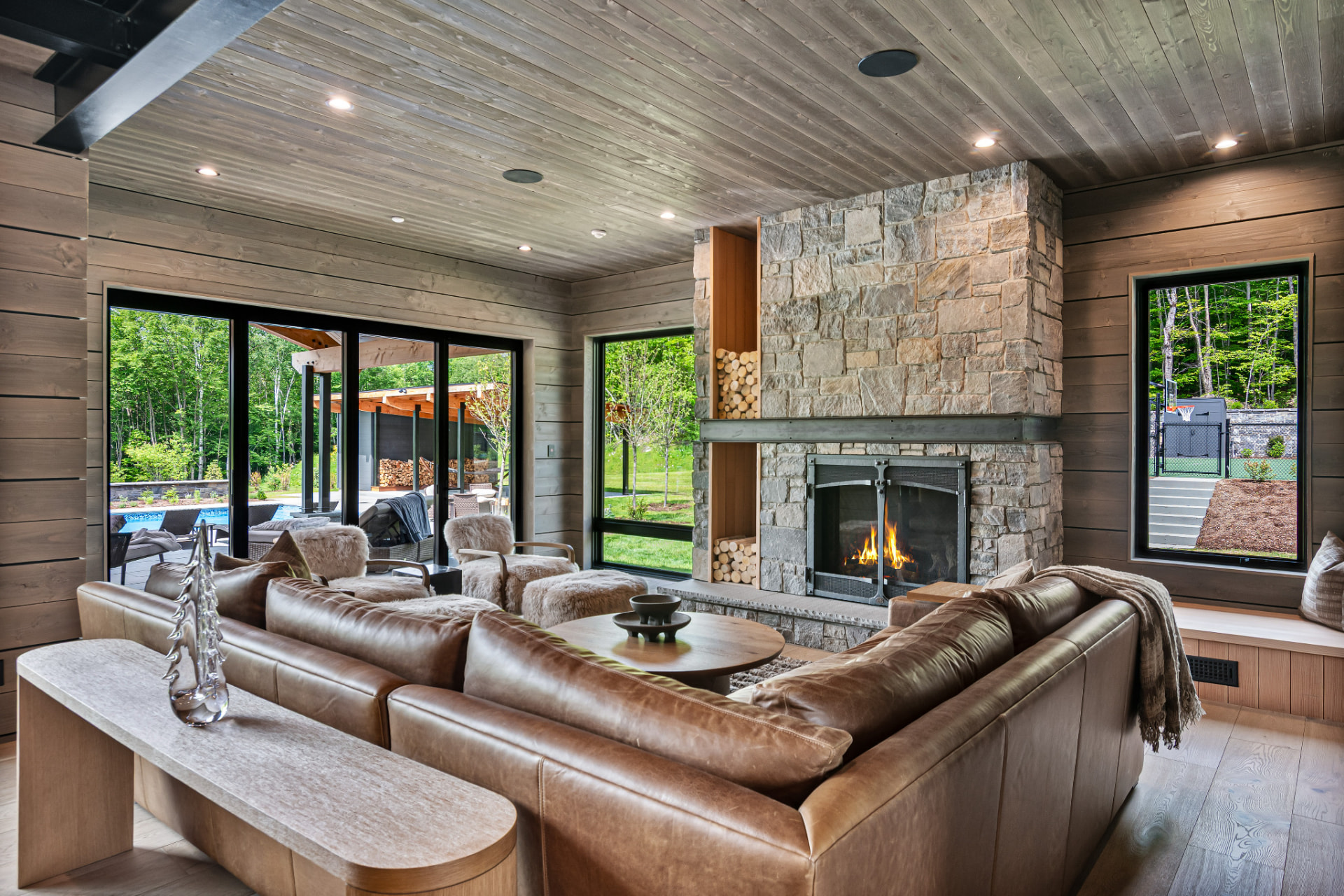 Living room with stone fireplace, wood ceiling, and leather seating